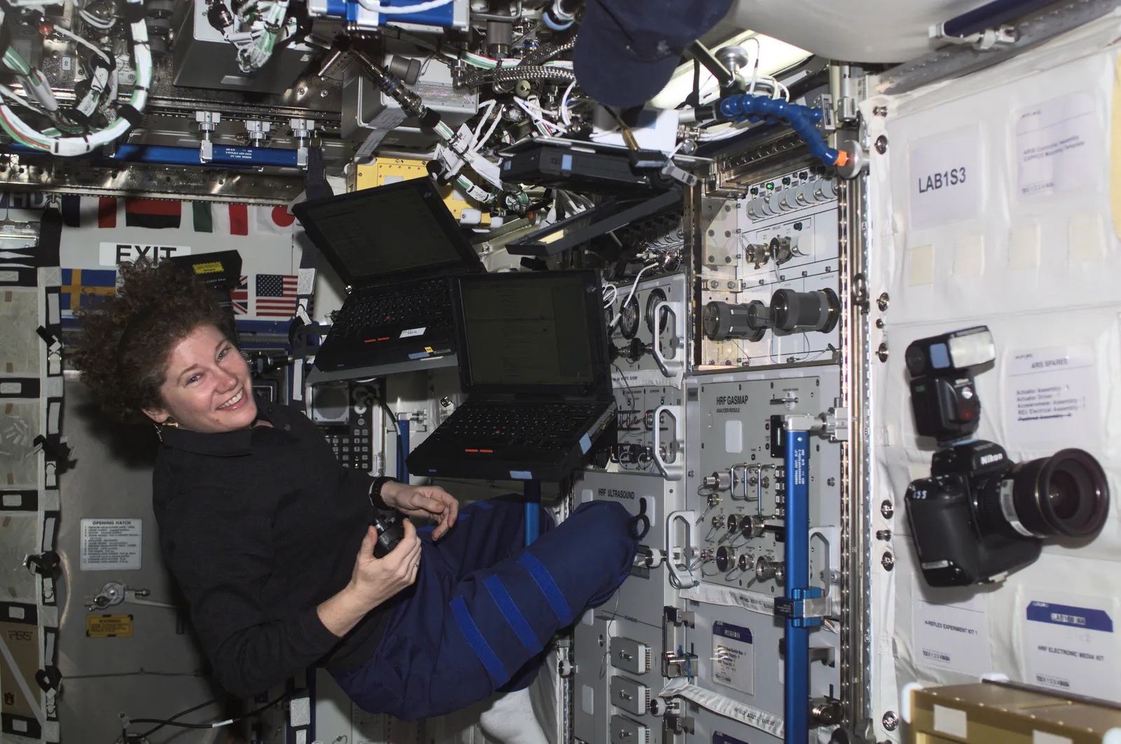 Astronaut Susan Helms smiling in the Space Station's Destiny laboratory, among three laptops fixed to the walls