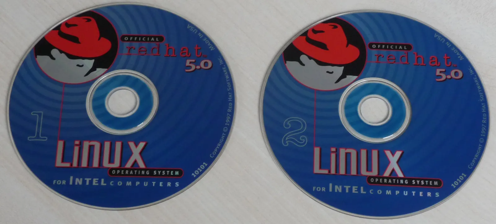 Two Red Hat Linux 5.0 CDs with the logo of the man in the red hat and the words Linux operating system for Intel computers