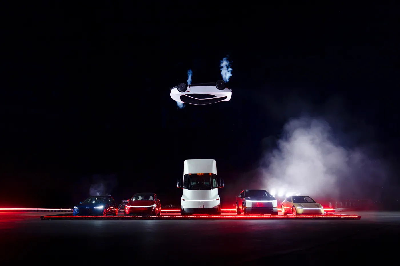 La nuova Tesla Roadster capovolta in aria sopra cinque Tesla parcheggiate, tra cui un camion Semi