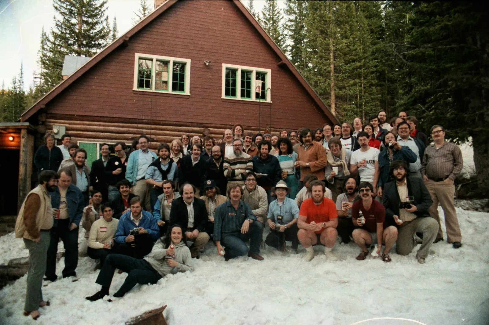 About thirty people posing on the snow in front of a wooden chalet; in the middle Dennis Ritchie, with glasses and a striped jumper